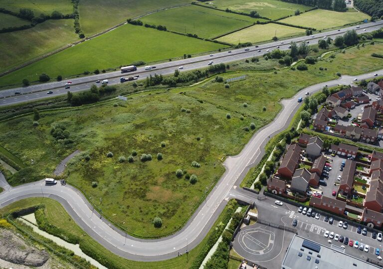 aerial view of a winding road cutting through green fields, next to a housing estate
