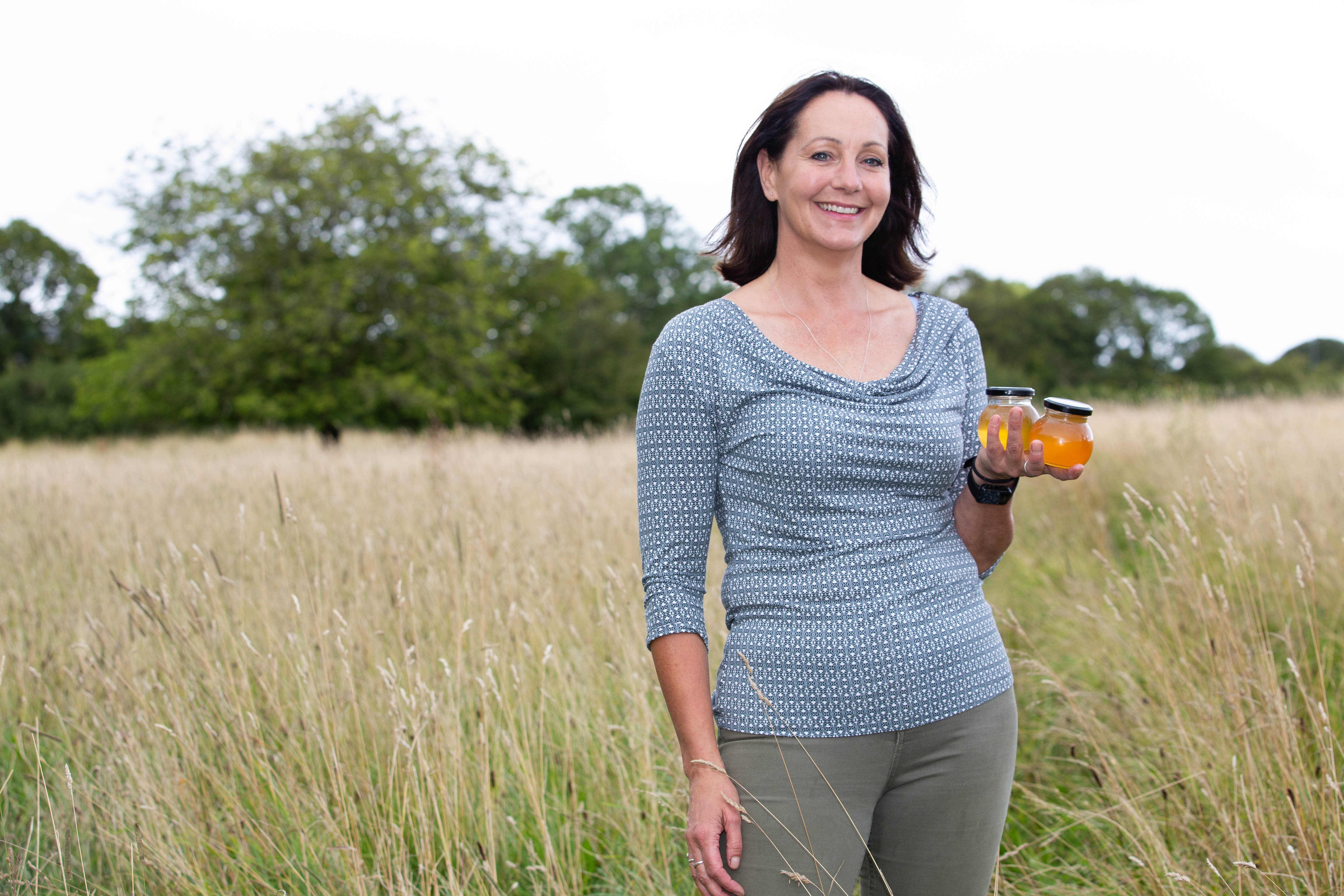 A woman standing in a field holding jars of honey