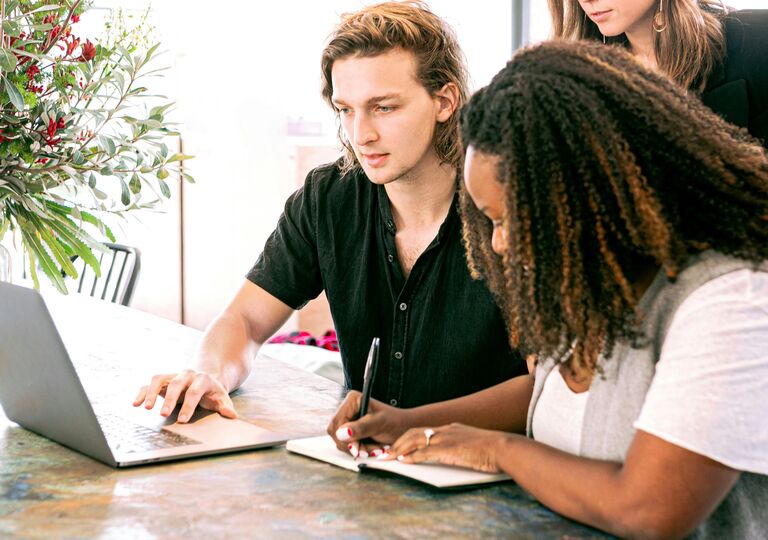A man looking at the laptop screen and a woman taking notes in the book