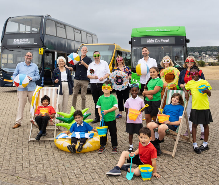 Group of kids and politicians, pose in front of buses reading 