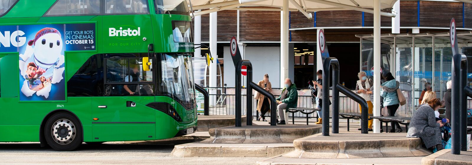 green bus pulling into station with people waiting