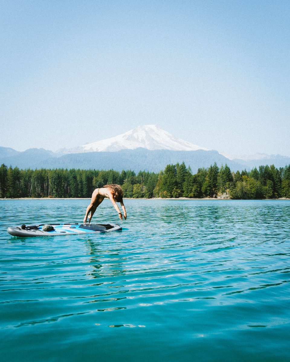 woman diving off paddle board large mountain in the background