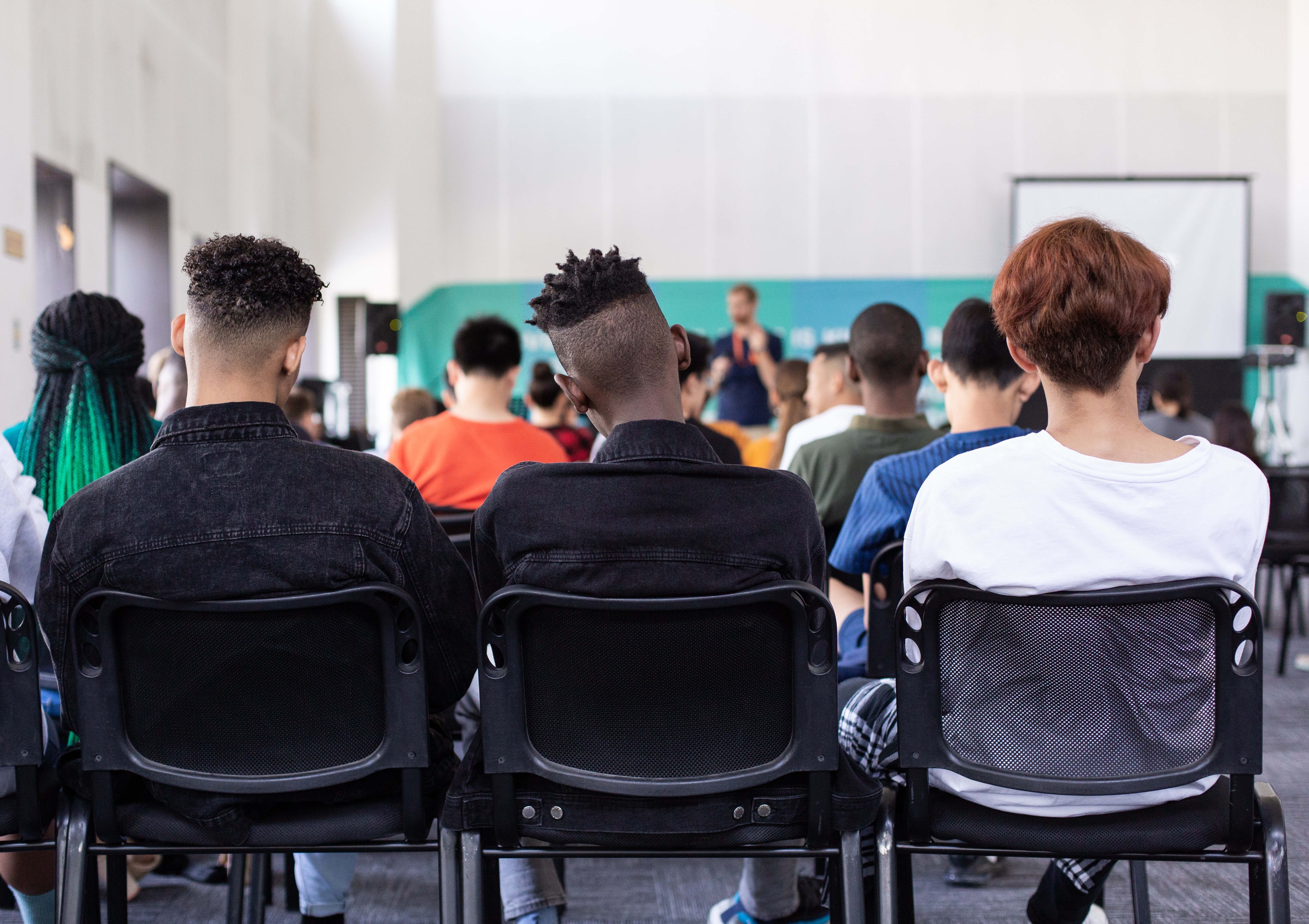 Students in class, image shows back of students as they face forwards towards the teacher. 