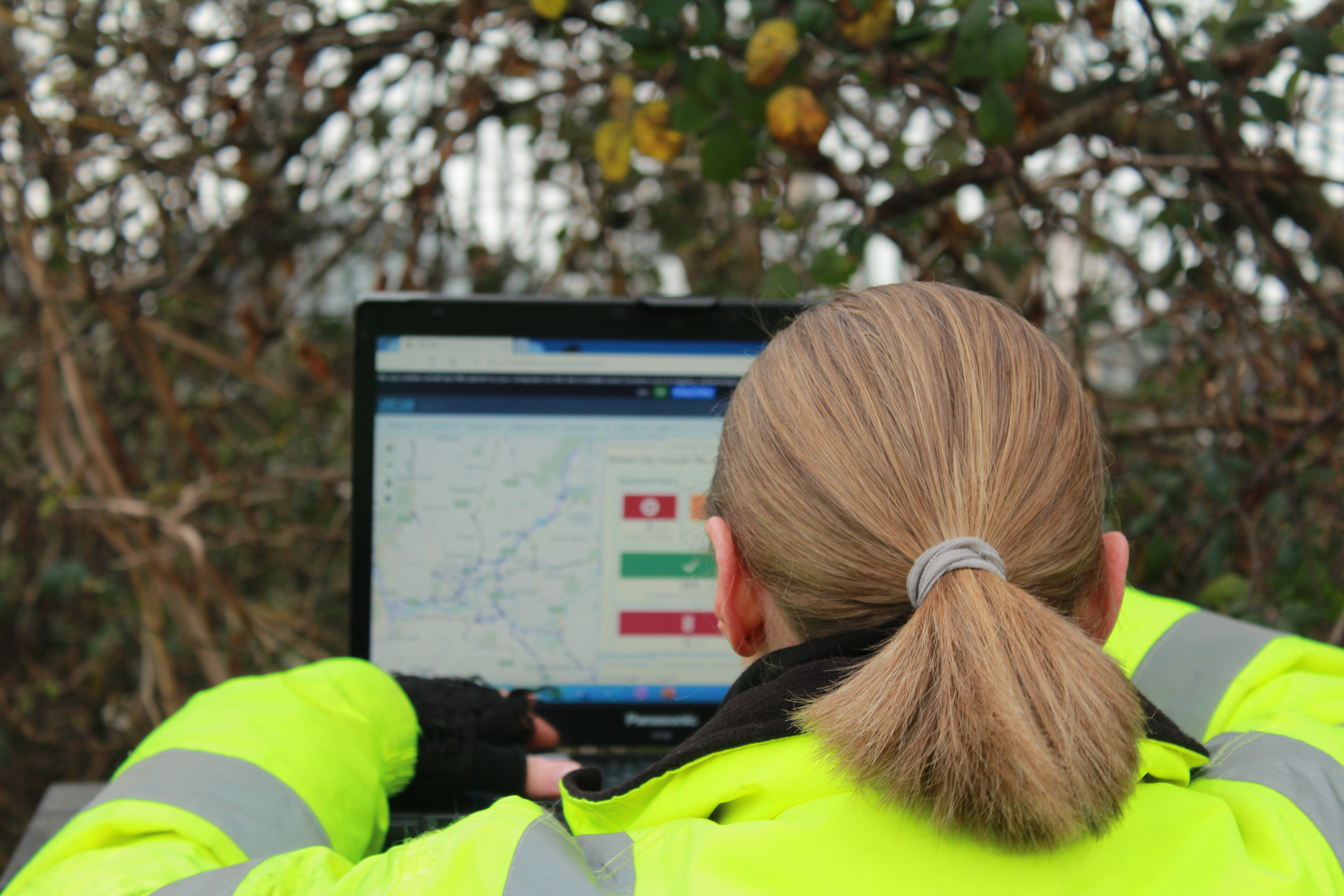 Woman in hi-vis jacket using laptop outside