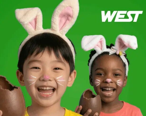 two children smiling, wearing bunny ears and holding up chocolate eggs