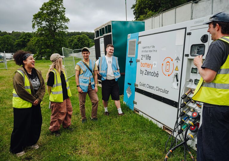 A group of people wearing high vis, standing around a large battery