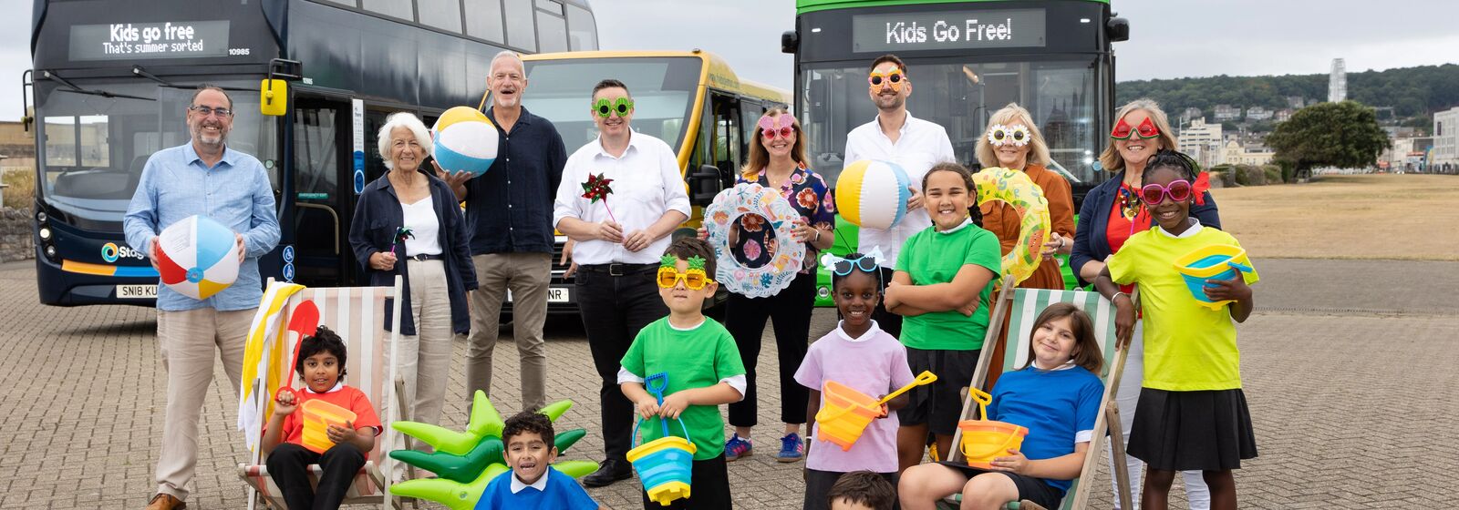 mayor, leaders and children with summer props in front of buses