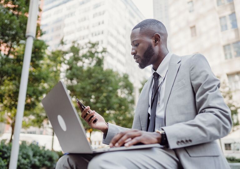 a man working on his laptop outside and looking at his phone