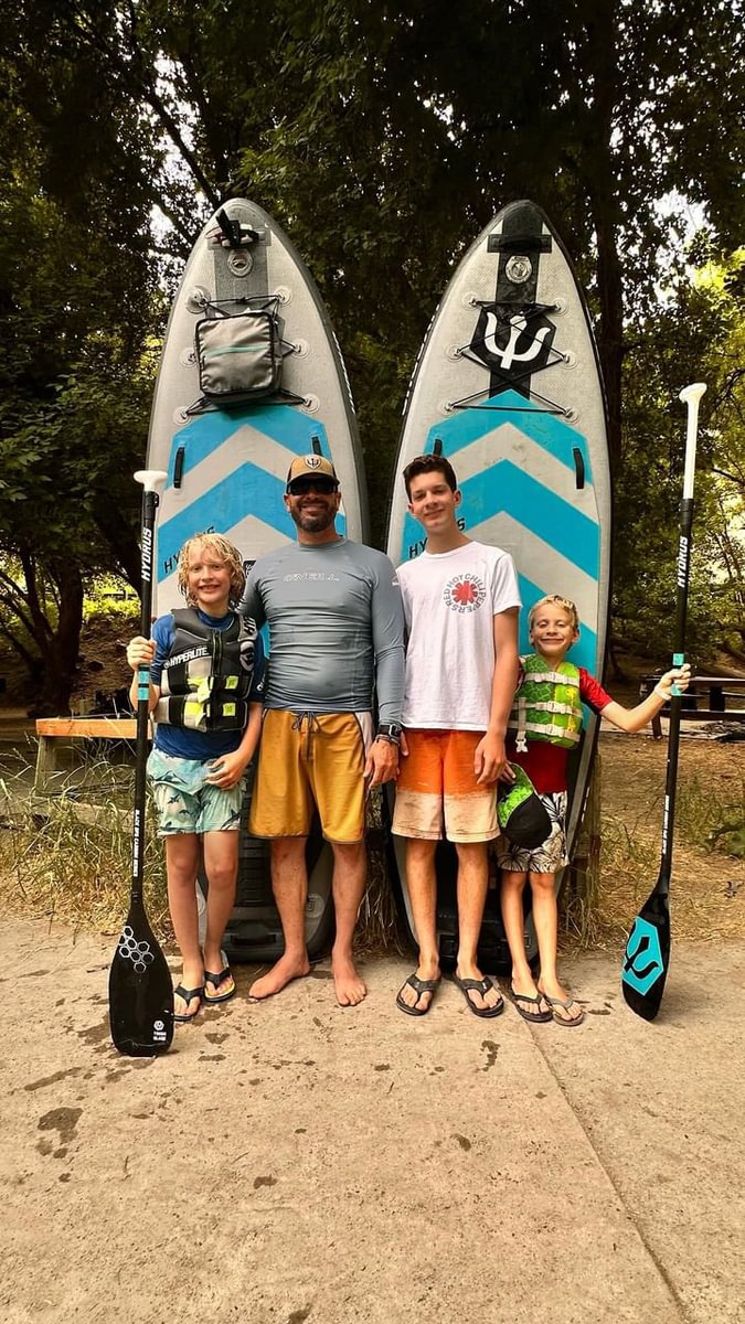 dad with three boys standing in front of two paddleboards