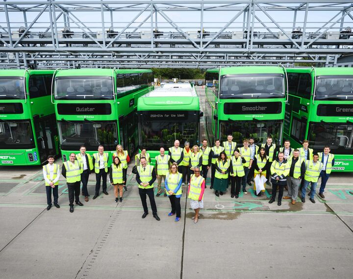 drone image of 4 buses and bus workers standing in from of them 