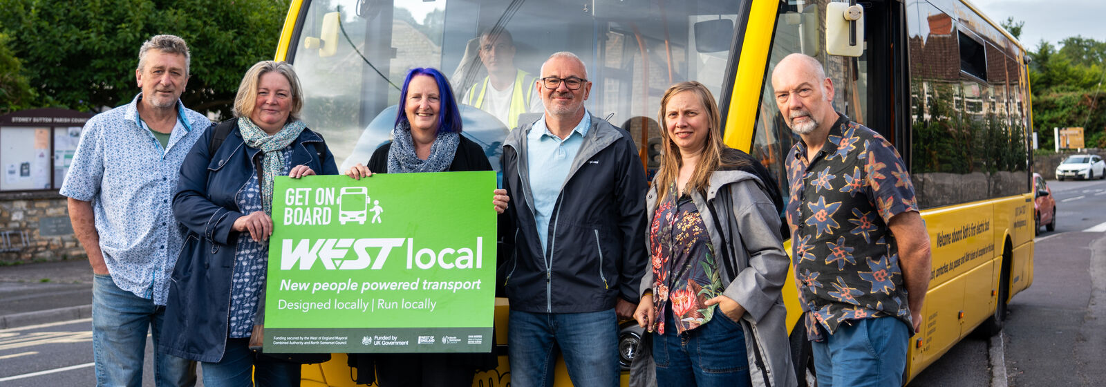 Local community group behind one of the WESTlocal schemes holding a WESTlocal people powered transport sign in front of their WESTlocal bus