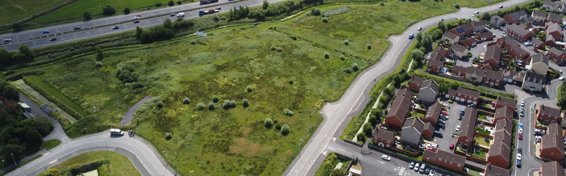 aerial view of road winding through green field, with houses on periphery