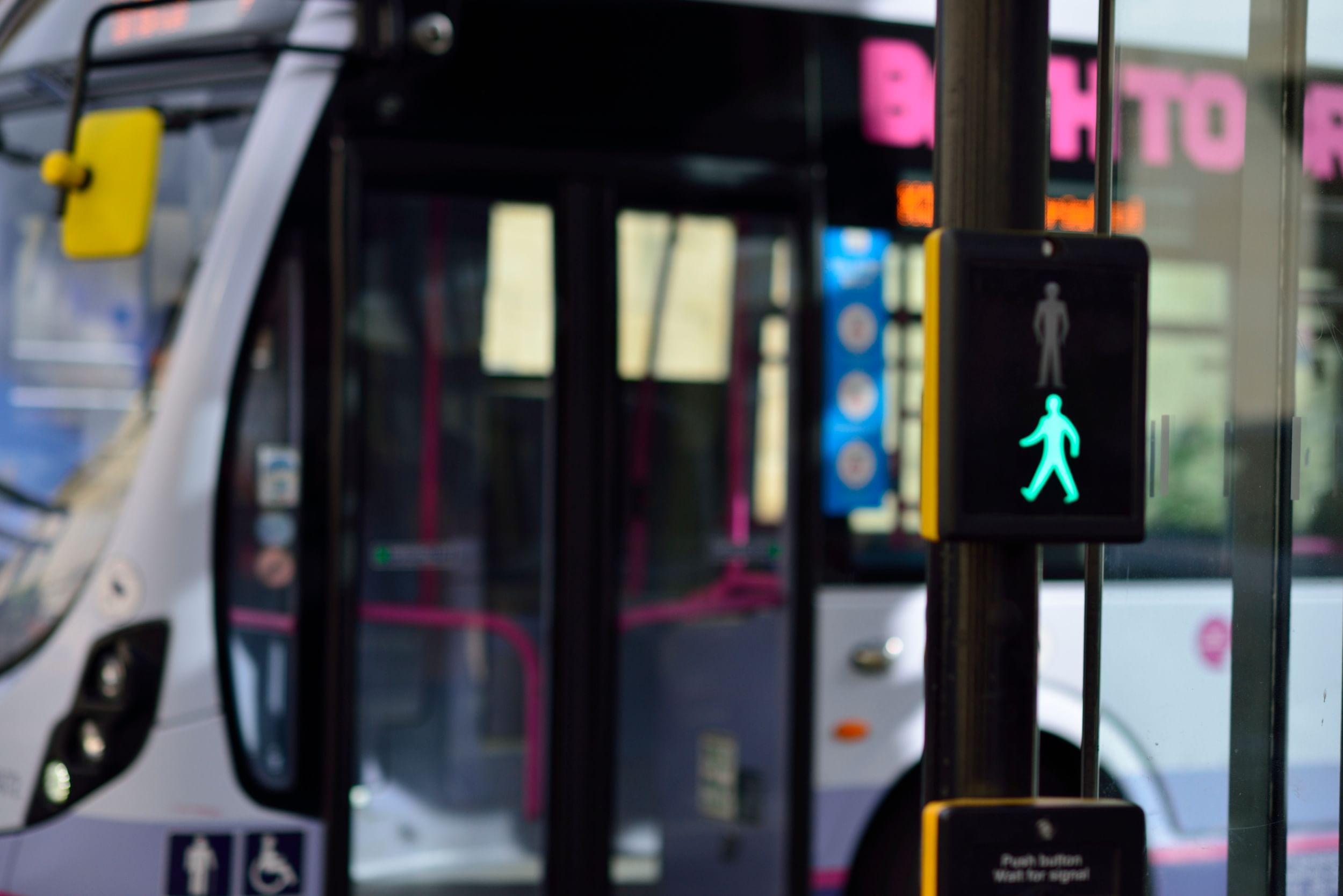 Pedestrian crossing light showing green light, with bus stopped behind it