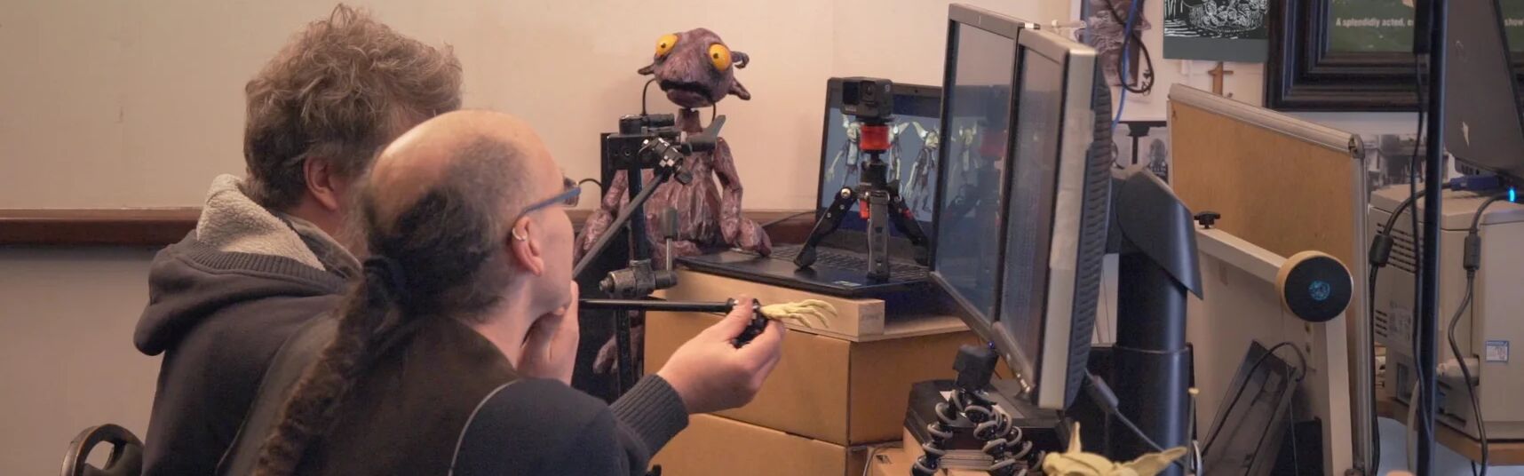 Two people working at a desk with screens and puppetry 