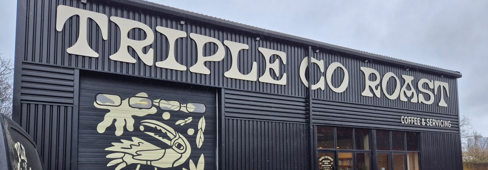 exterior of black building with cream sign reading 'triple co roast, coffee and servicing'