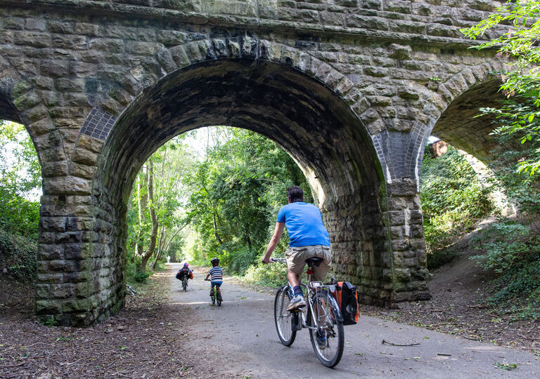 A man and two young children cycling under a viaduct