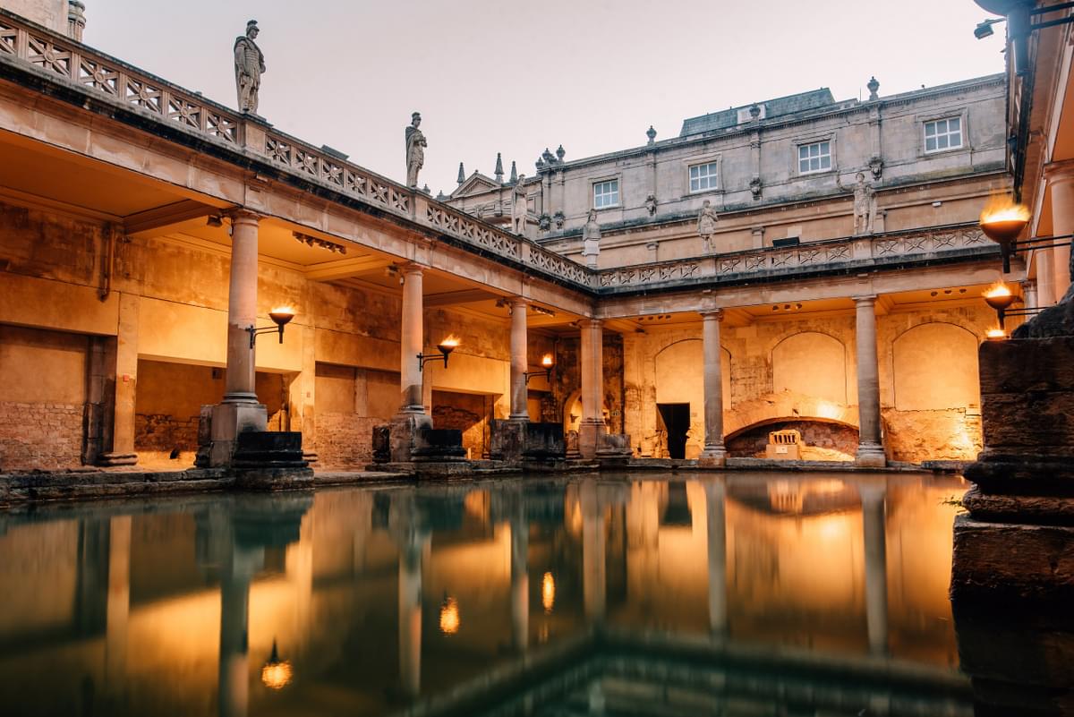 Roman baths at night - with orange light, the domes of the baths and water at the forefront