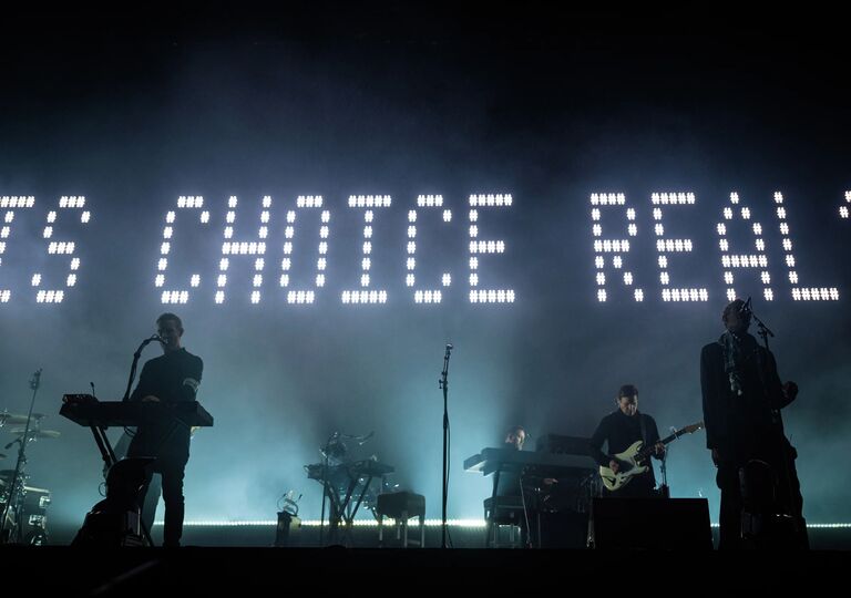 people on stage at night, backlit by writing that says 'is choice real?'