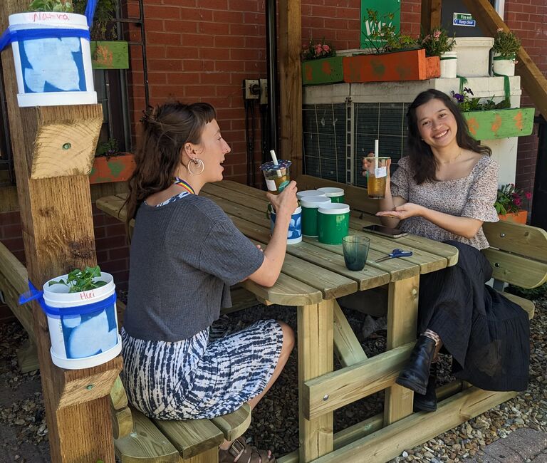 Two people drinking at a bench