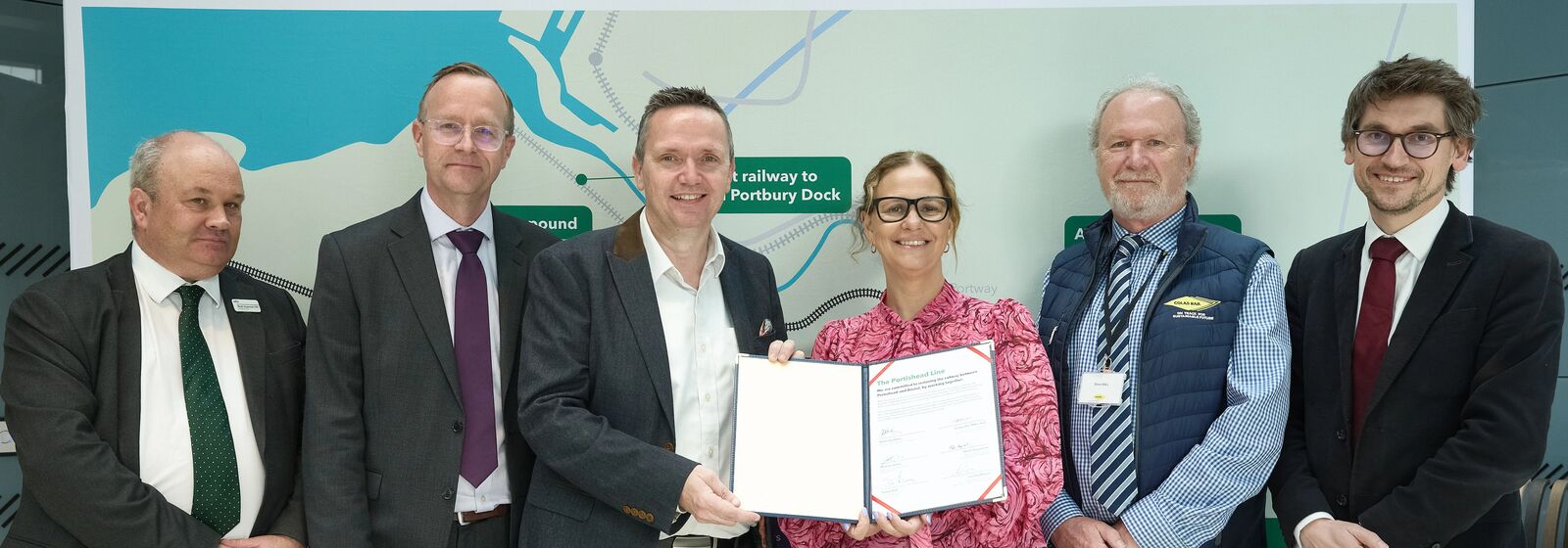 Mayor is stood in front of a map holding a contract. Delivery partners stand either side of her