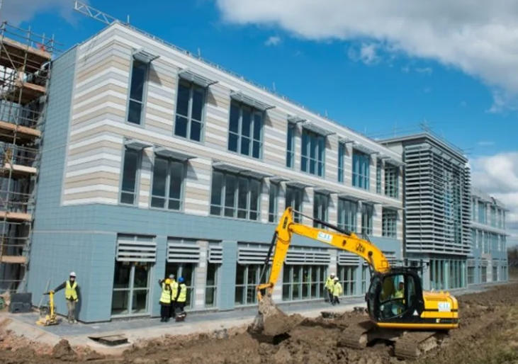 workmen and a yellow digger in front of a partially constructed building