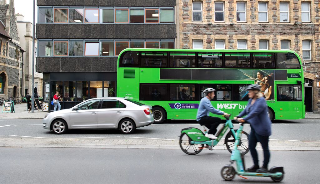 Scooter, cyclist, bus, car and walker all going down a road