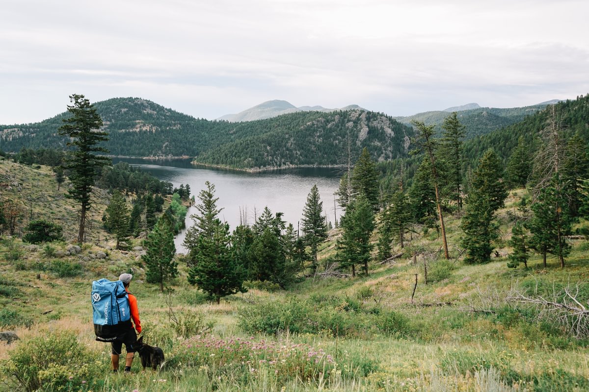man hiking with paddleboard in a backpack overlooking a lake