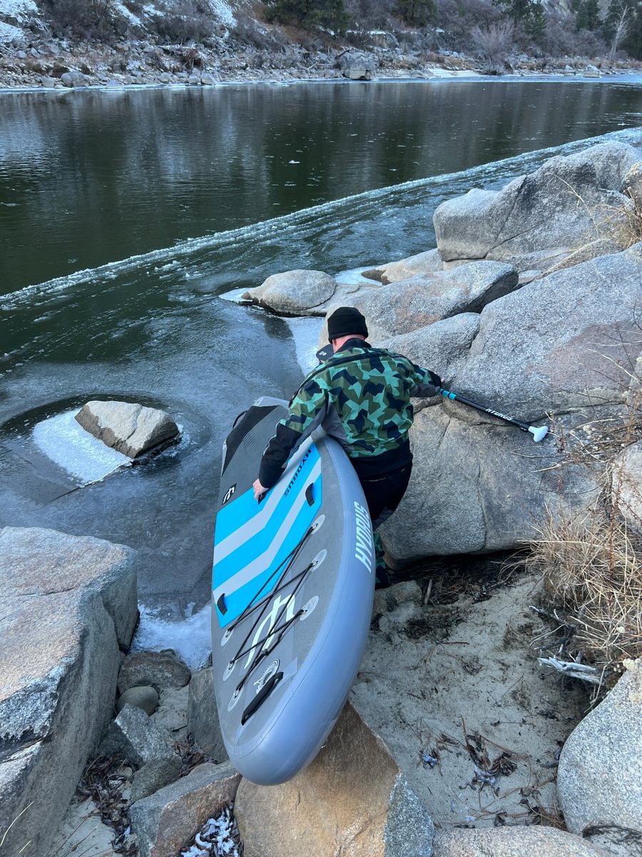 man in drysuit with paddleboard getting in icy water