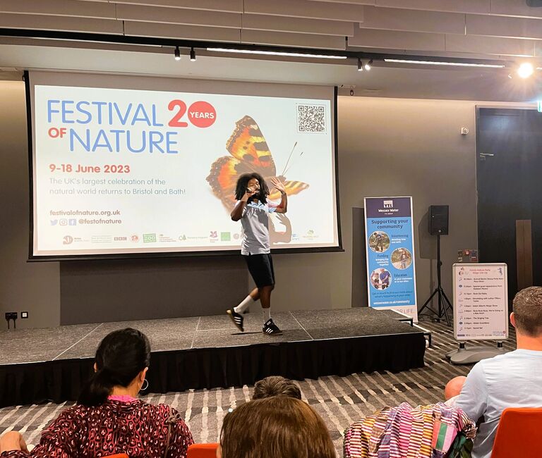 Person on stage in front of a screen saying 
