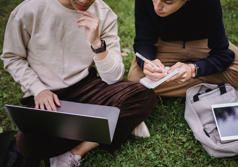 Two people looking at the laptop screen and taking notes 