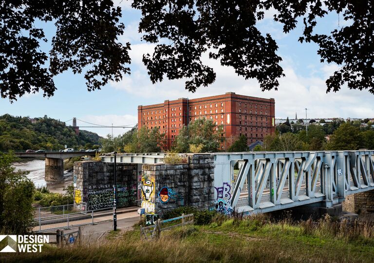 view of graffiti covered bridge with large orange building and clifton suspension bridge in the background