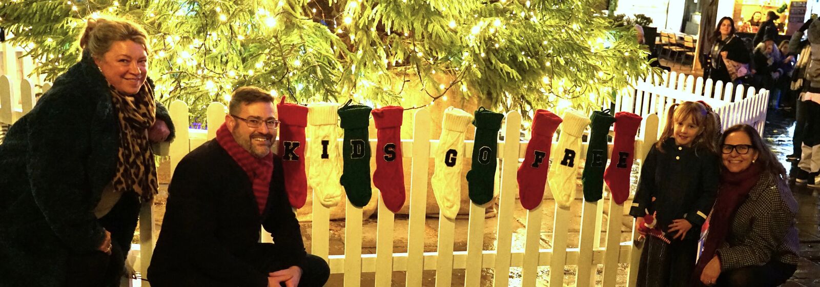 Mayor Helen Godwin, Councillor Kevin Guy, Kathryn Davis, and Olive are pictured with Christmas stockings spelling out Kids Go Free in front of the Christmas Tree at Bath Christmas Market.