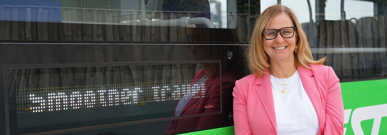 Mayor Helen Godwin stands next to a green bus with a sign that reads 'Smoother travel'