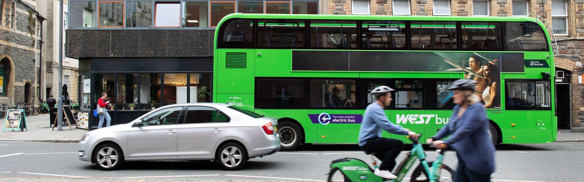 Bus, cyclist, scooter and car driving past 