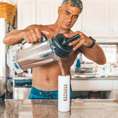 Fit gray haired man in kitchen pouring chocolate shake from blender into a white Ka'Chava bottle