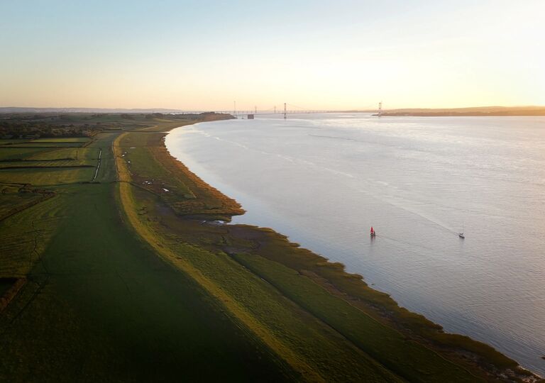 photo of river severn with red-sailed boat and severn crossing in the distance