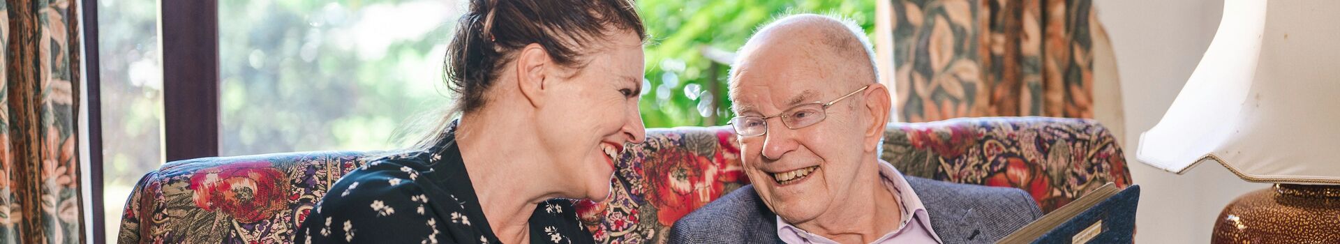 Older person reading at sofa with a carer