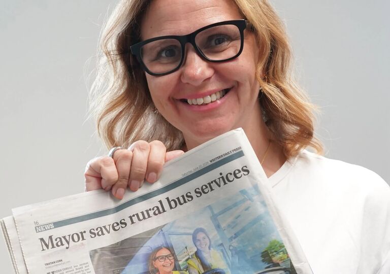 Myor Helen Godwin holds up a newspaper with headline that reads 'Mayor saves rural bus services'