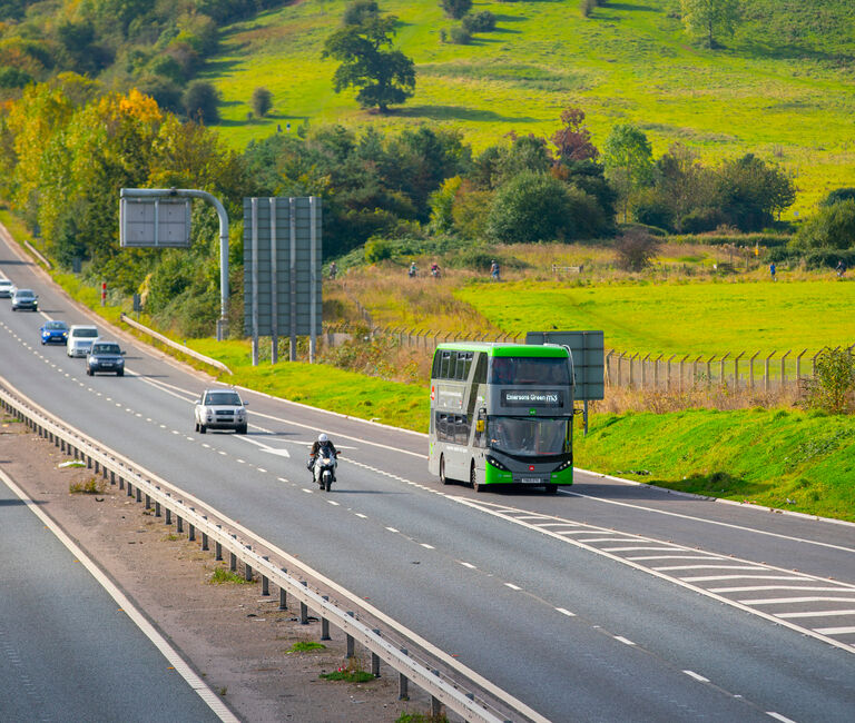 Metrobus driving along motorway, cars around, fields in background