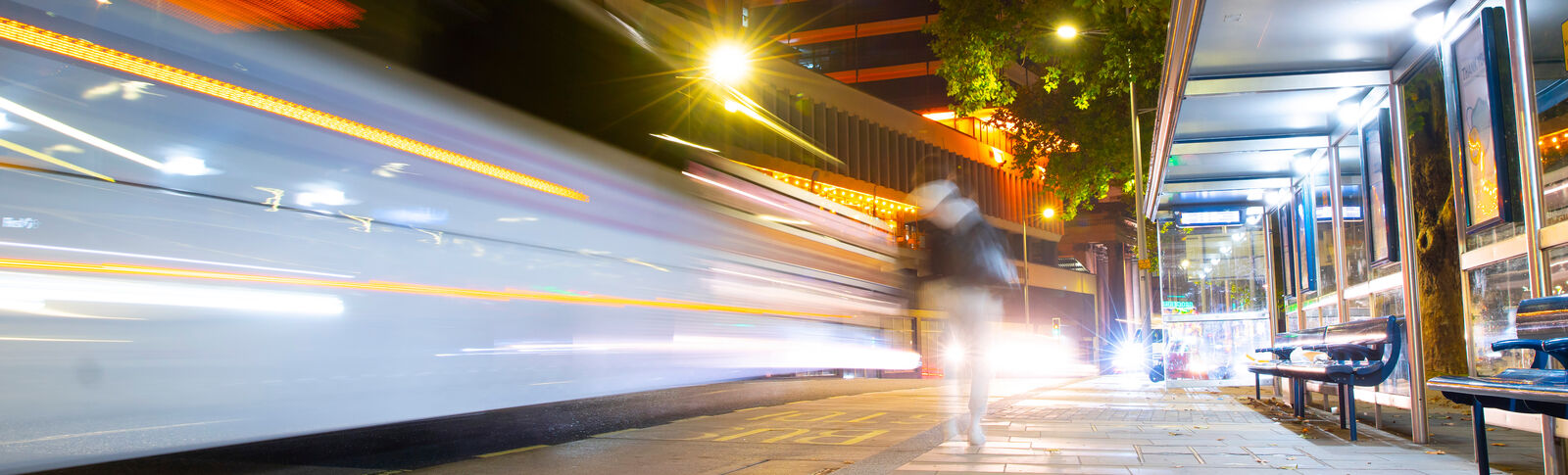 Night time scene of bus passing a bus stop and person walking
