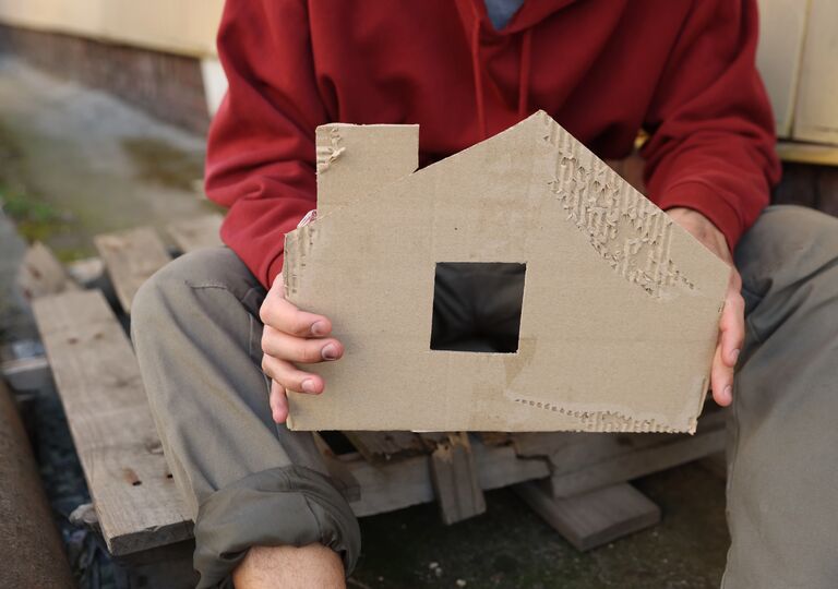 a homeless person holding up a piece of cardboard in the shape of a house