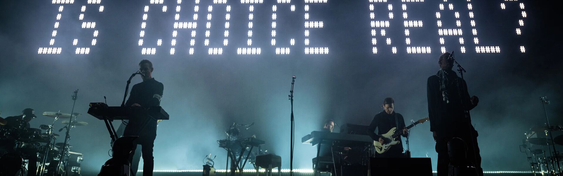 people on stage at night, backlit by writing that says 'is choice real?'